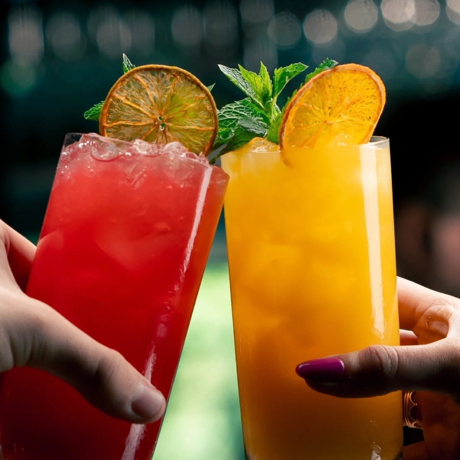 Two colourful iced drinks garnished with citrus and mint
